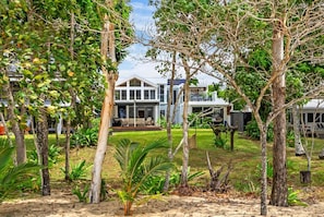 A residential property with a large house, a covered outdoor seating area, and a well-maintained garden with various plants. - Belle Escapes Beach Villa San Remo (Holloways Beach)