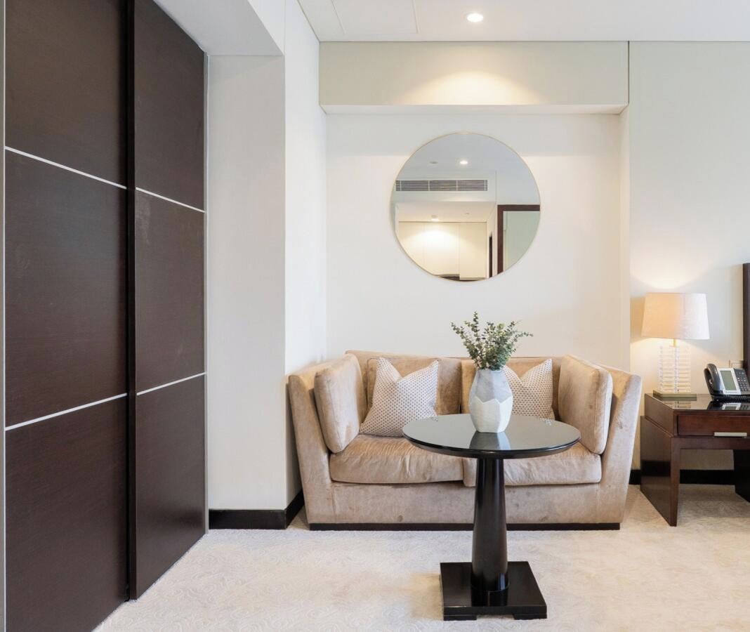 Ein Hotelzimmer mit einer Couch, einem runden Tisch mit einer Vase, einer Lampe und einem Spiegel an der Wand.
