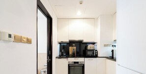 A compact kitchen with a microwave, oven, and a coffee maker on the countertop. - The Grand • Luxury Oasis at JW Marriott (Dubai)