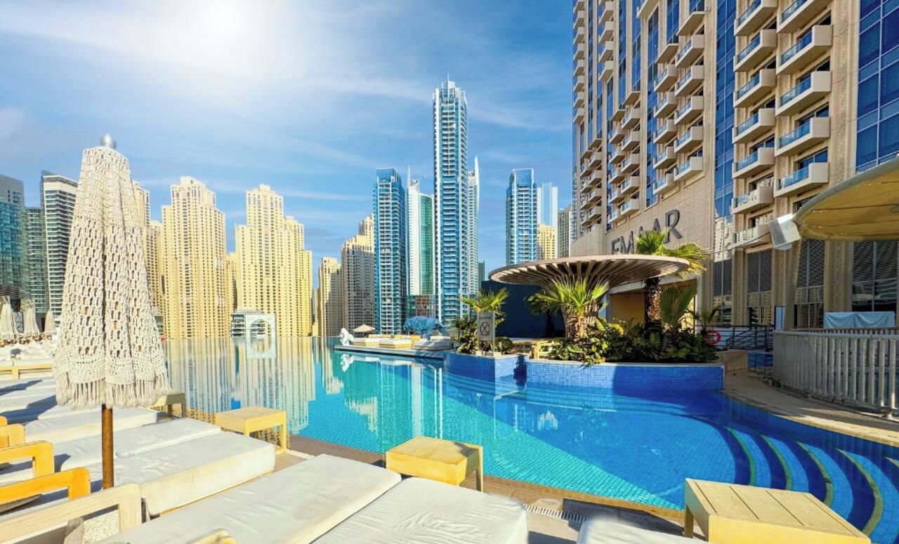 A pool area with lounge chairs, a water feature, and a city skyline in the background.