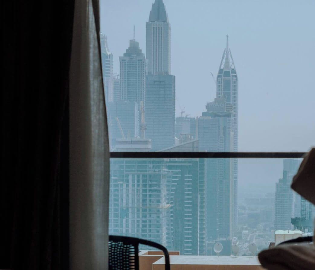 A view of a cityscape through a window with a chair visible in the foreground.