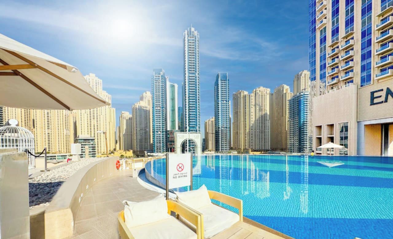 A swimming pool with a 'NO DIVING' sign, surrounded by high-rise buildings and a clear sky.