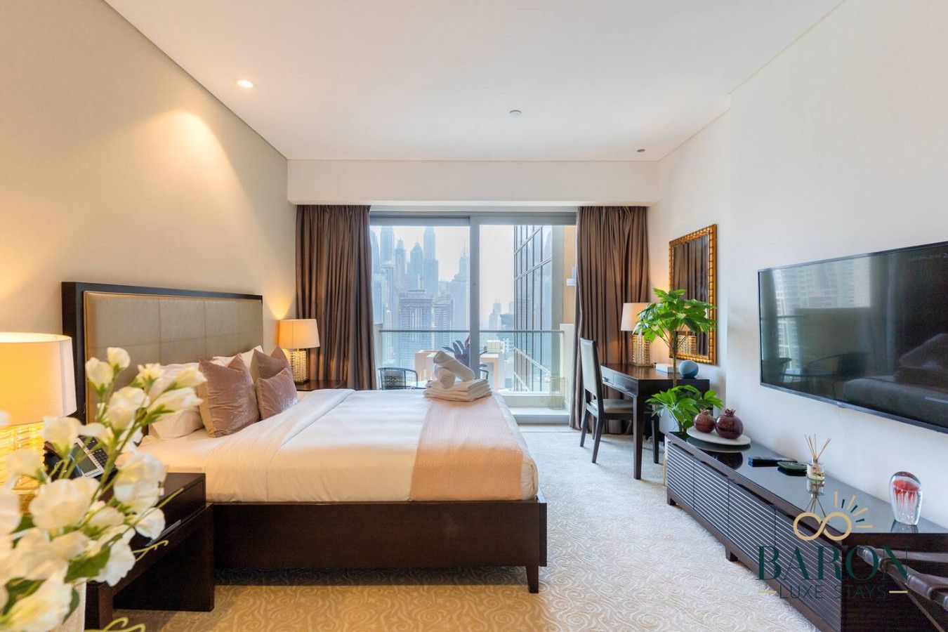 Ein modernes Hotelzimmer mit einem großen Bett, einem Flachbildfernseher, einem Schreibtisch mit Stuhl und Blick auf die Stadtlandschaft durch das Fenster.