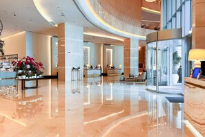 A modern hotel lobby with a reception desk, seating area, and a glass partition. - The Majestic • JW Marriott (Dubai)