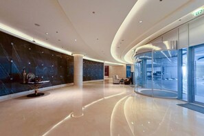 A modern lobby with a curved ceiling, a glass elevator, and a marble wall. - The Majestic • JW Marriott (Dubai)