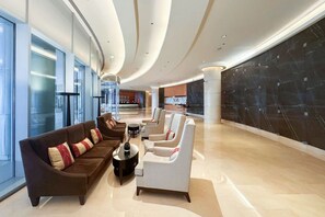 Eine geräumige Lobby mit modernem Design, inklusive einer Sitzecke mit Sofas und Sesseln, einem Empfangsbereich und einer großen Marmorwand.