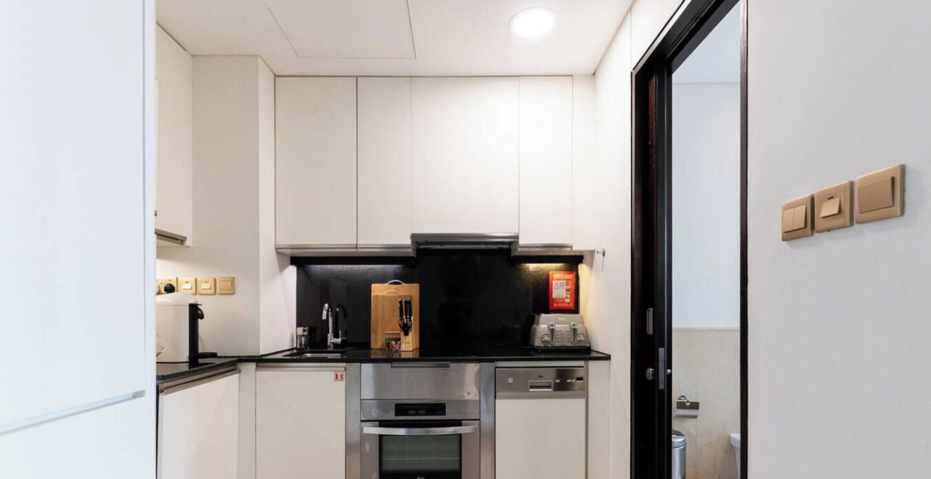 A compact kitchen with white cabinets, a black countertop, a built-in oven, and a dishwasher.