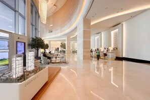 A spacious hotel lobby with a modern design, featuring a reception desk, seating areas, and a large window overlooking the street. - The Serene • JW Marriott (Dubai)