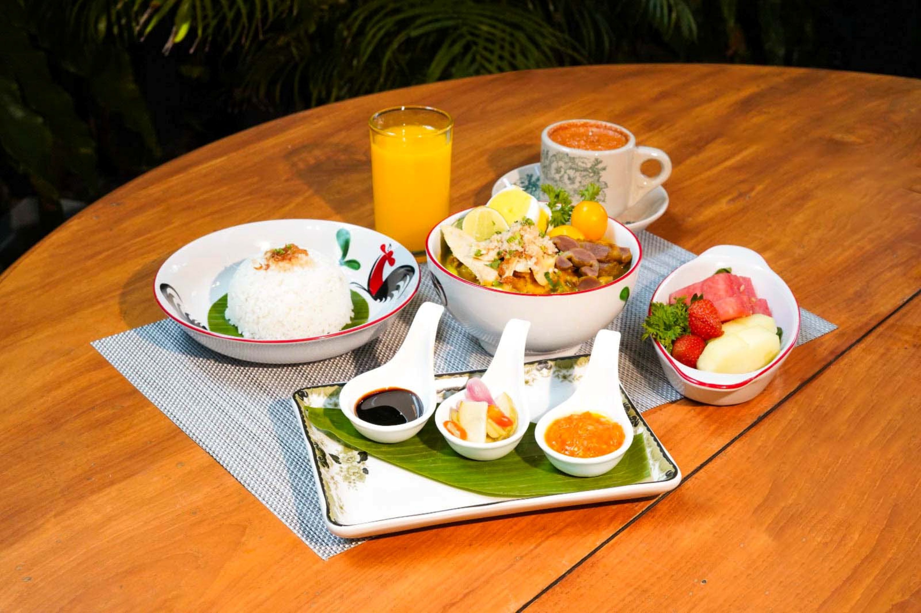 A table with a meal consisting of rice, soup, and various side dishes, along with a glass of orange juice and a cup of coffee.