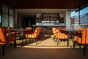 Een moderne eethoek met oranje stoelen en tafels, een keuken op de achtergrond en een balkon met een hekwerk.