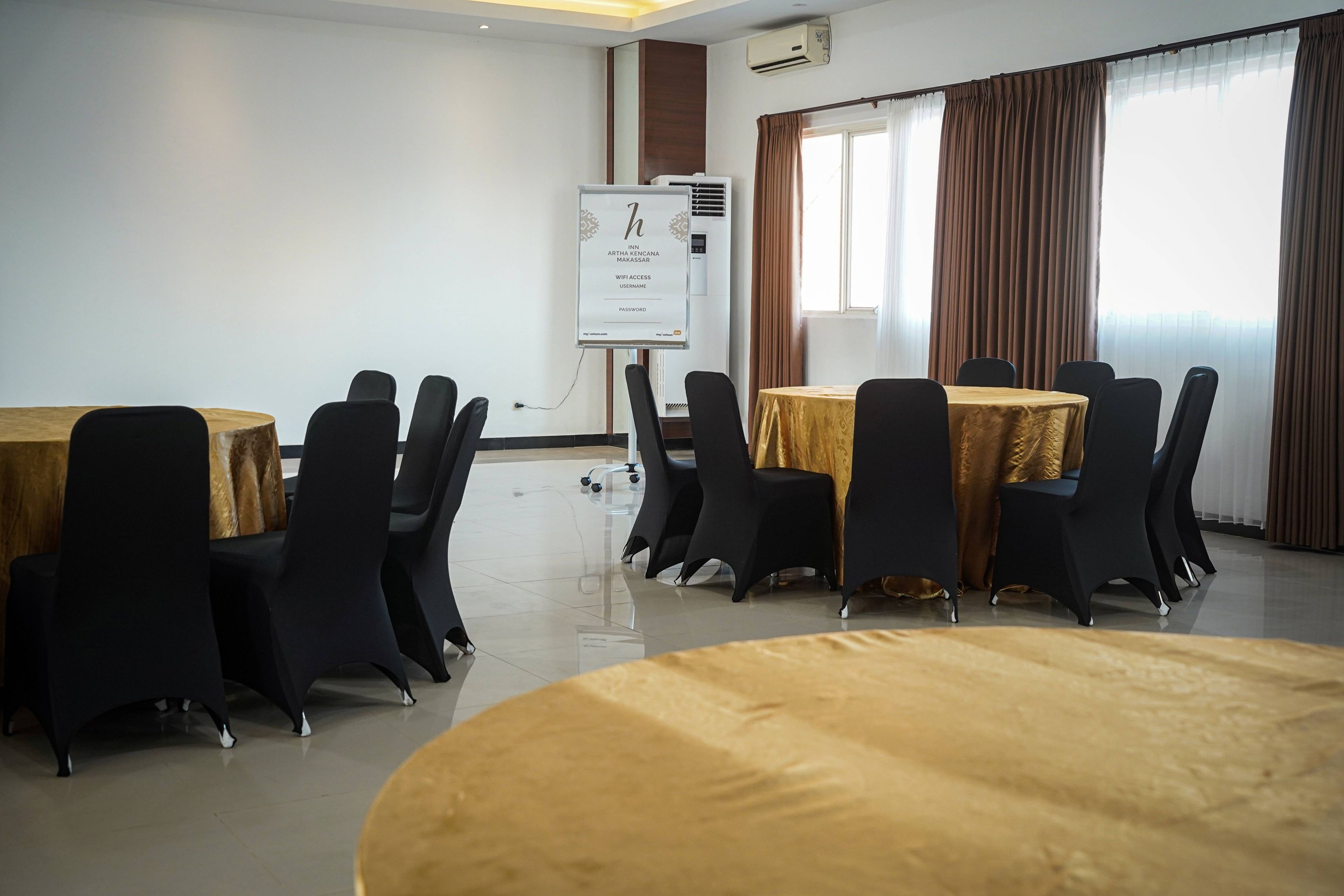 Ein Konferenzraum mit runden Tischen, schwarzen Stühlen, einer Whiteboard-Tafel und einer Klimaanlage.