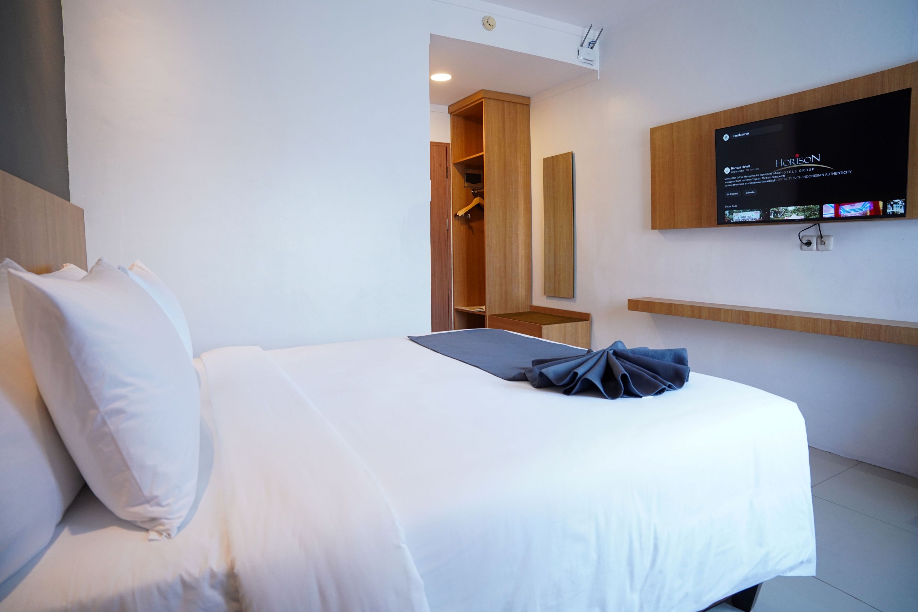 Une chambre d’hôtel avec un lit, un téléviseur fixé au mur, une armoire en bois et une petite table.