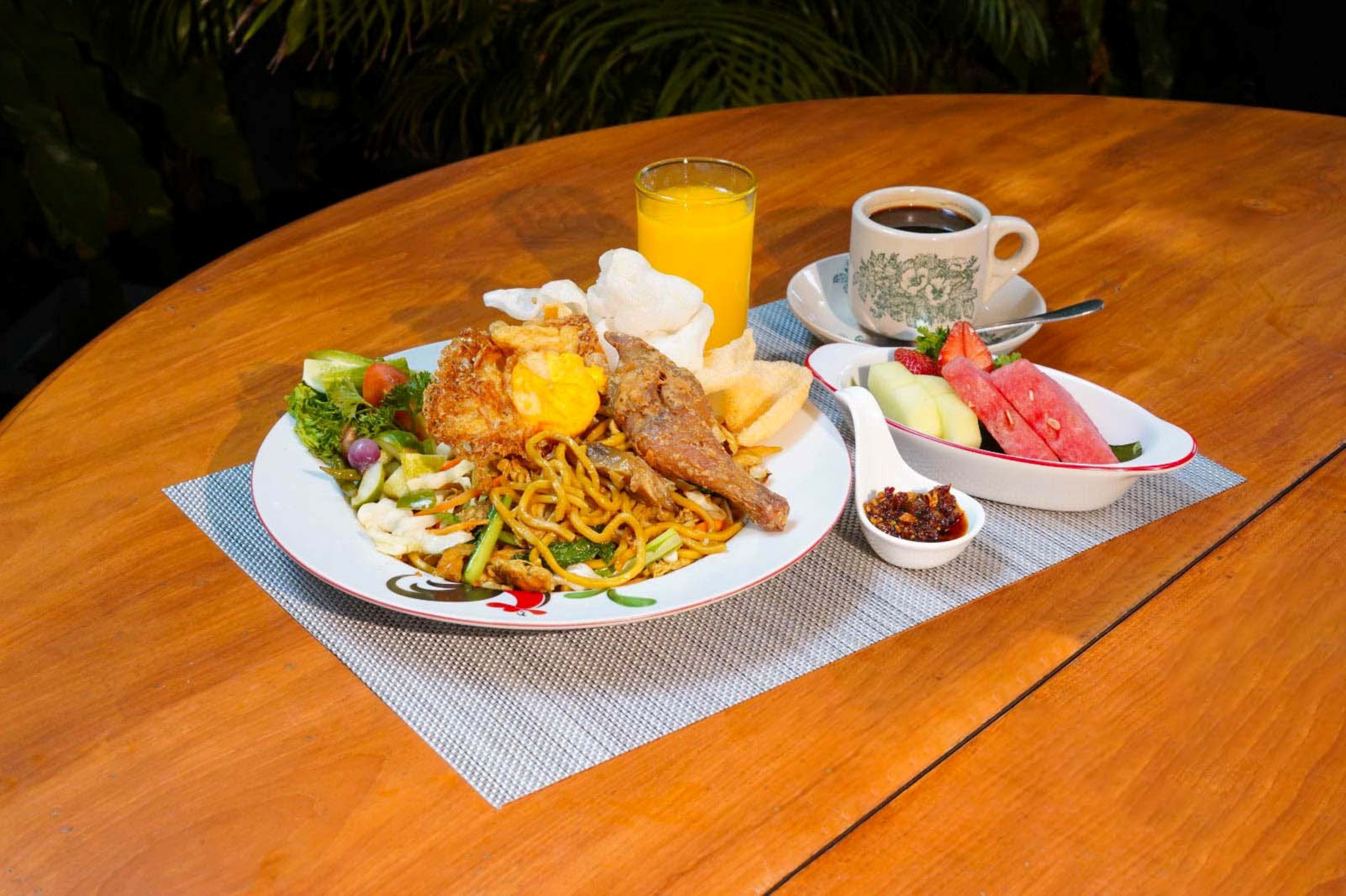 A round wooden table with a plate of food, a glass of orange juice, a cup of coffee, and a bowl of fruit.