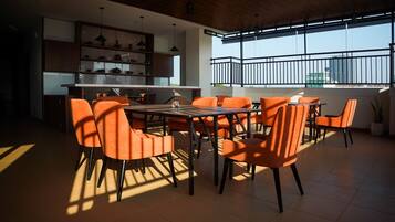 A dining area with a large table and chairs, a kitchen area with cabinets and shelves, and a view through a window with a railing.