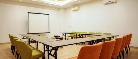Un salón de conferencias con una mesa larga, varias sillas, una pantalla de proyector y luces en el techo.