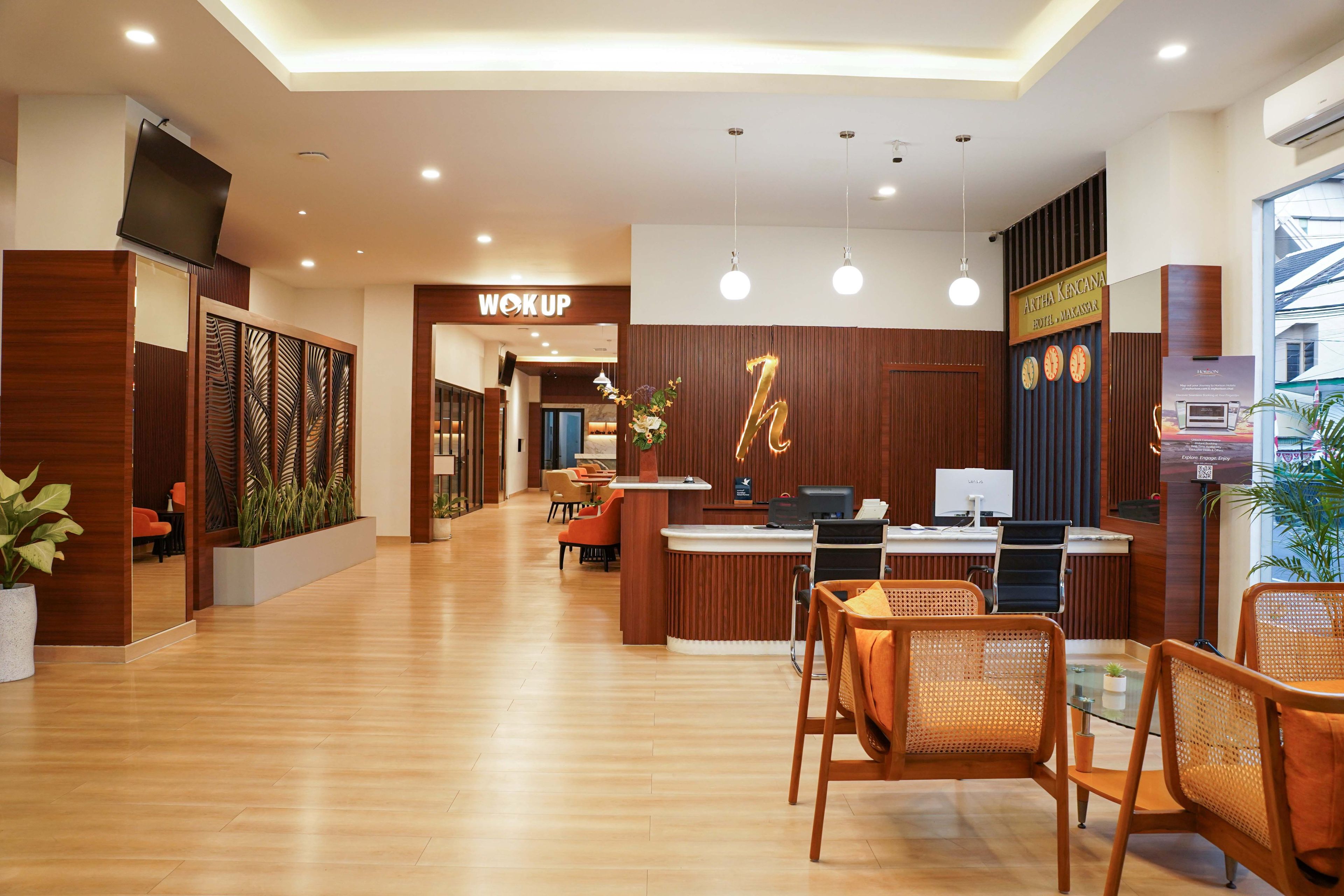 Zona de recepción de un hotel con mostrador, área de estar y un letrero que dice 'WOK UP'.