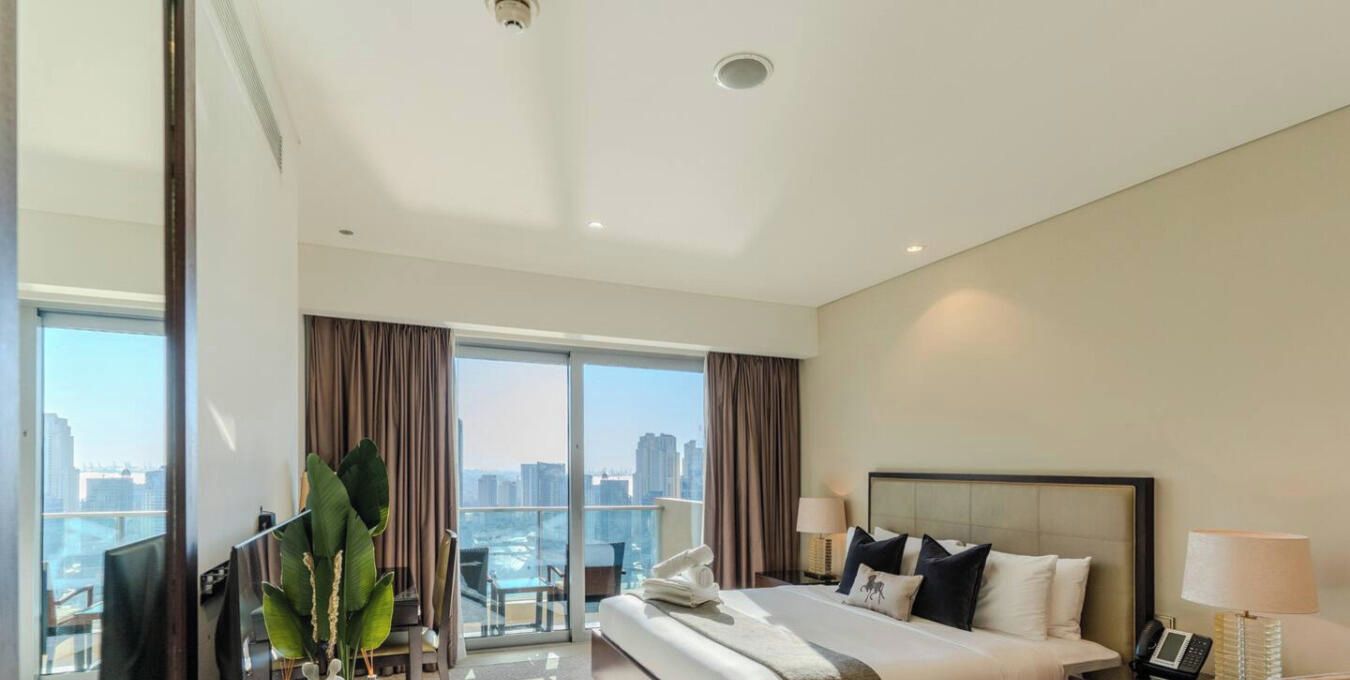 Une chambre d’hôtel moderne, dotée d’un grand lit, d’un bureau et offrant une vue sur le paysage urbain.