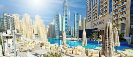 A rooftop pool area with lounge chairs and umbrellas, surrounded by high-rise buildings.