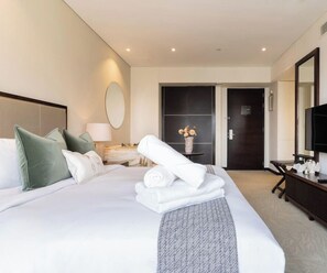 A hotel room with a bed, a desk, a mirror, and a TV. - The Classy • JW Marriott (Dubai)