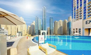 A swimming pool area with a 'NO DIVING' sign, surrounded by high-rise buildings and a clear sky. - The Cozy • JW Marriott (Dubai)