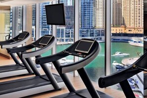 A gym with treadmills and a large window overlooking a marina and buildings. - The Cozy • JW Marriott (Dubai)