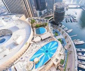 Un hotel frente al agua con una amplia piscina central, varios balcones y un puerto deportivo con barcos.