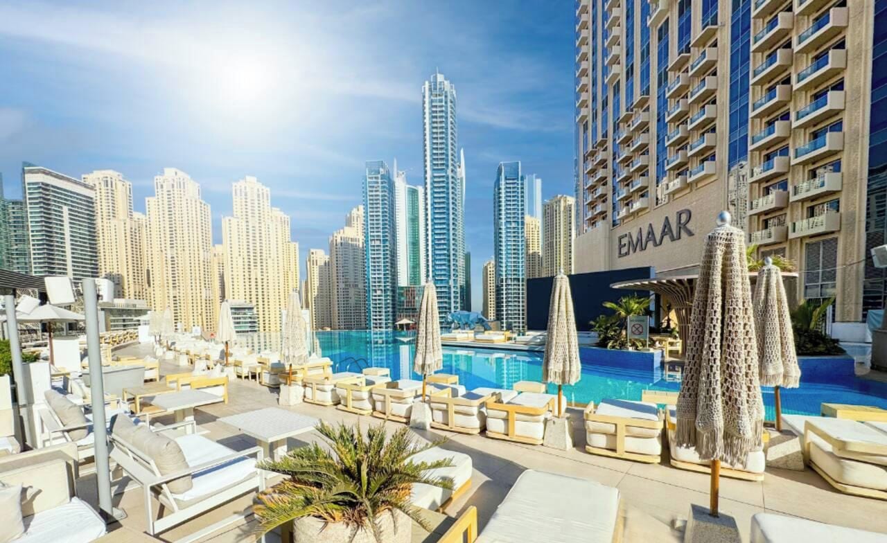 A rooftop pool area with lounge chairs and umbrellas, surrounded by high-rise buildings.