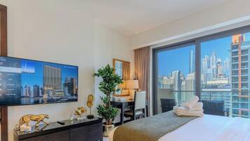 Habitación de hotel con un ventanal grande, cama, escritorio, televisor y vista a la ciudad.