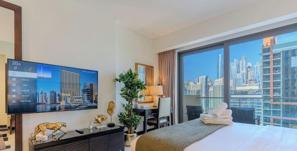 Habitación de hotel con un ventanal grande, cama, escritorio, televisor y vista a la ciudad.