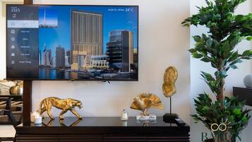 Un televisor mostrando un paisaje urbano con una pantalla de información de hotel, una figura dorada decorativa de un animal y una planta en maceta.