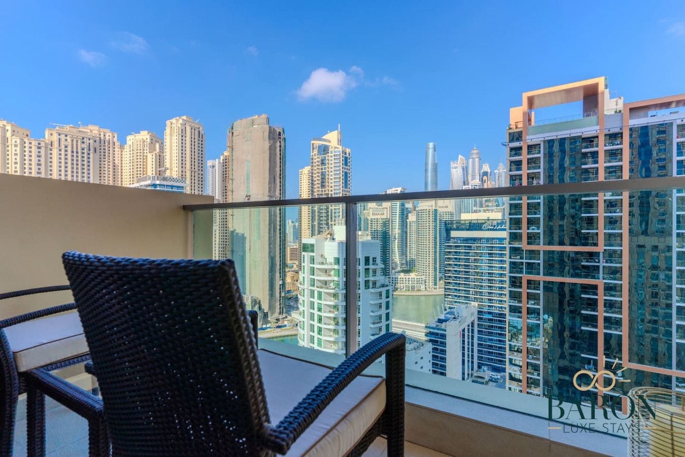 A balcony with a view of a city skyline, a wicker chair, and a glass railing.
