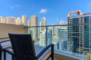 Un balcón con vistas a un horizonte urbano, una silla de mimbre y una barandilla de cristal.