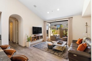 A modern living room with a flat-screen TV, leather sofa, and a dining area with a coffee table. - 3-bedroom estate in SantaLuz Community  with AC and fitness room and Spa (San Diego)