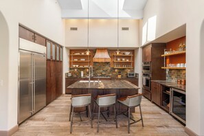 A modern kitchen with a central island, bar stools, stainless steel appliances, and a brick backsplash. - 3-bedroom estate in SantaLuz Community  with AC and fitness room and Spa (San Diego)