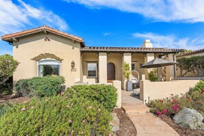 A two-story house with a tiled roof, a front porch, and a garden with flowering plants. - 3-bedroom estate in SantaLuz Community  with AC and fitness room and Spa (San Diego)