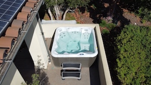Een hottub met een opstap, omringd door een tuin en een gebouw.