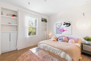 Een slaapkamer met een bed, een raam, een plank met planten en een kunstwerk aan de muur.