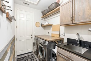 Een kleine wasruimte met een wasmachine, een wasbak en houten kastjes.