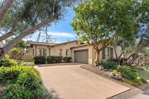 A two-story house with a covered driveway, surrounded by mature trees and well-maintained landscaping. - 3-bedroom estate in SantaLuz Community  with AC and fitness room and Spa (San Diego)