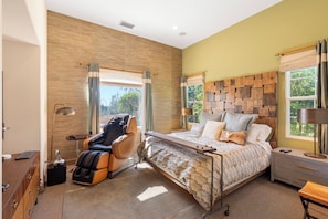 A bedroom with a massage chair, a bed with a patterned bedspread, a headboard with a brick-like design, and a view of greenery outside. - 3-bedroom estate in SantaLuz Community  with AC and fitness room and Spa (San Diego)