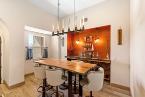 A dining area with a wooden table and four chairs, a bar with bottles, and pendant lighting. - 3-bedroom estate in SantaLuz Community  with AC and fitness room and Spa (San Diego)