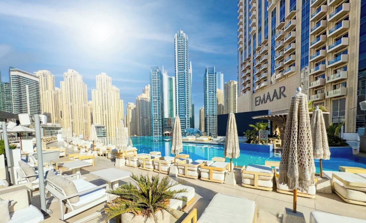 A rooftop pool area with lounge chairs and umbrellas, surrounded by high-rise buildings.