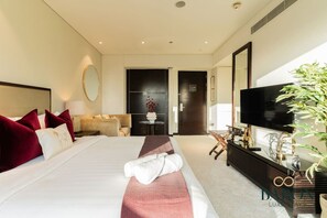 A modern hotel room with a large bed, a television, a sofa, and a mirror. - The Captivating • JW Marriott (Dubai)