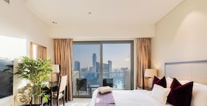 Ein Hotelzimmer mit Bett, Schreibtisch, Stuhl, einer Pflanze und Blick auf eine Stadtlandschaft.