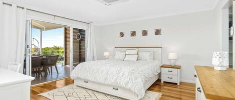 A bedroom with a bed, bedside tables, a nightstand, a wooden floor, a patterned rug, and a view through a sliding door to an outdoor area.