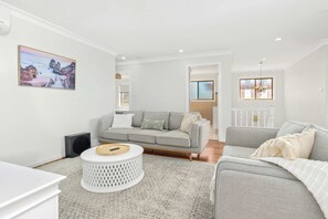 A modern living room with a grey sofa, a white coffee table, and a painting of a coastal scene. - Callala Beach Walk - Beachfront with Sauna (Callala Beach)