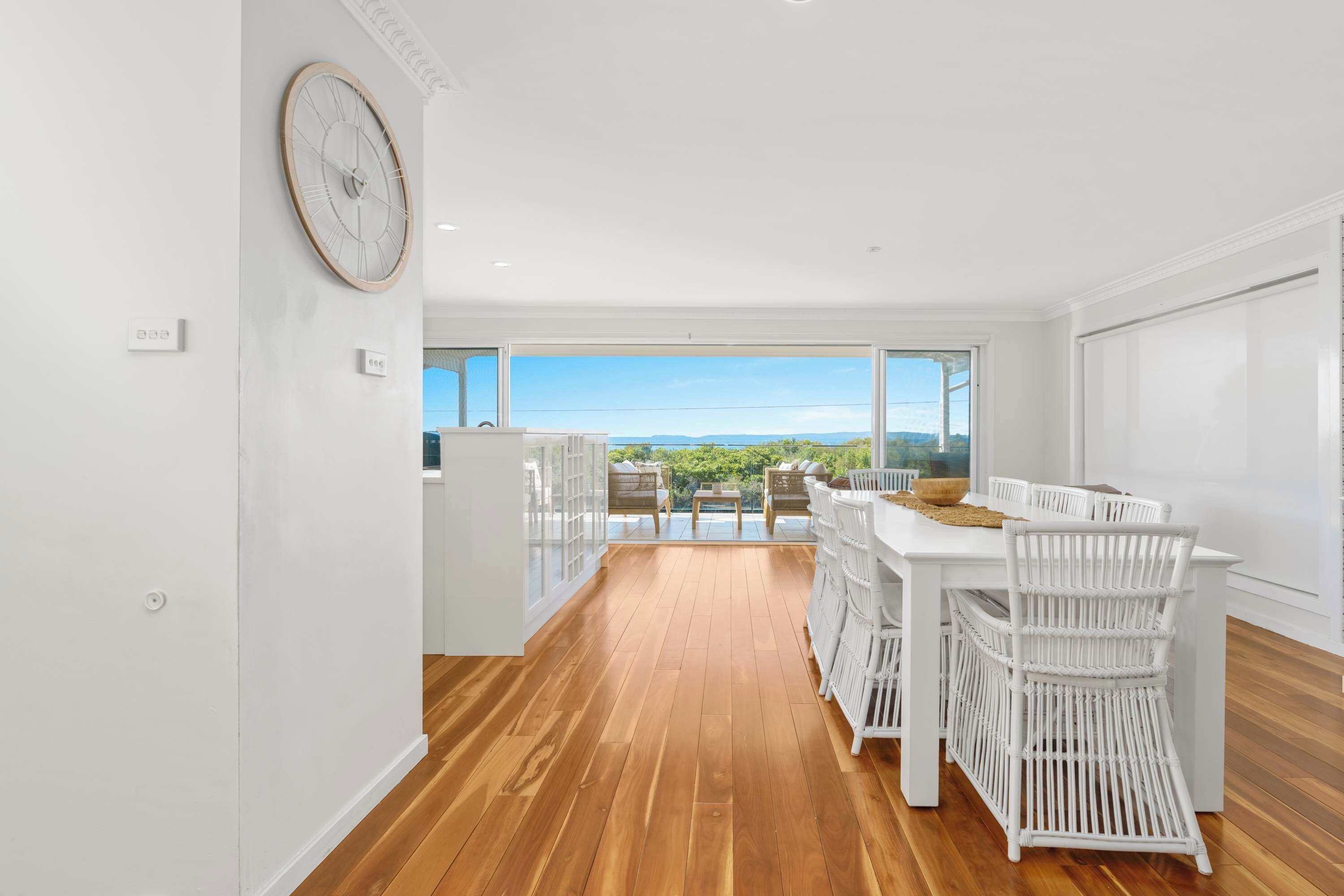 A modern kitchen with a large window, wooden flooring, and white furniture.
