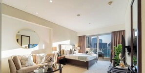 Ein Hotelzimmer mit einem großen Bett, einem Sofa, einem runden Spiegel und einem Balkon mit Blick auf die Stadt.
