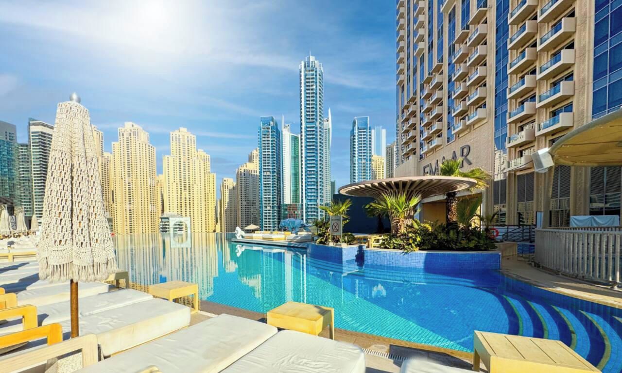A pool area with lounge chairs, a water feature, and a city skyline in the background.
