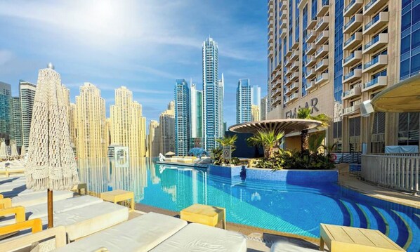 A pool area with lounge chairs, a water feature, and a city skyline in the background. - The Spectacular • JW Marriott (Dubai)